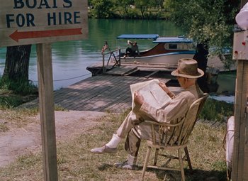 Movie still from “Niagara” (1953), directed by Henry Hathaway – An older man sitting in a chair reading a newspaper; Wide shot, High angle