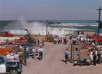 Movie still from “Niagara” (1953), directed by Henry Hathaway – A group of people standing on top of a sandy beach; Extreme Wide shot, High angle