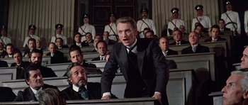 Movie still from “Nicholas and Alexandra” (1971), directed by Franklin J. Schaffner – A man in a suit and tie standing in front of a group of men; Medium shot, Low angle