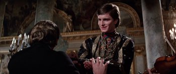 Movie still from “Nicholas and Alexandra” (1971), directed by Franklin J. Schaffner – A young man in a black and gold outfit holding a pair of scissors in his hand; Medium shot, Over the shoulder angle