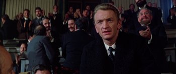 Movie still from “Nicholas and Alexandra” (1971), directed by Franklin J. Schaffner – A man in a suit and tie in front of a group of people; Close Up shot, Over the shoulder angle