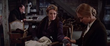 Movie still from “Nicholas and Alexandra” (1971), directed by Franklin J. Schaffner – An older woman sitting at a table with a cross on her chest; Medium shot, Over the shoulder angle