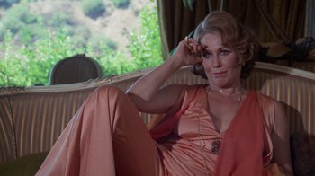 Movie still from “Night Moves” (1975), directed by Arthur Penn – A woman sitting on a couch in a living room; Medium shot, High angle