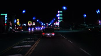 Movie still from “Night Moves” (1975), directed by Arthur Penn – Cars driving down a street at night with a mcdonald's sign in the background; Extreme Wide shot, High angle