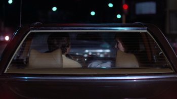 Movie still from “Night Moves” (1975), directed by Arthur Penn – Two people sitting in the back seat of a car at night; Medium shot, Over the shoulder angle