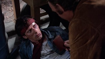 Movie still from “Night Moves” (1975), directed by Arthur Penn – A man in a red tie is sitting on the ground; Close Up shot, Overhead angle