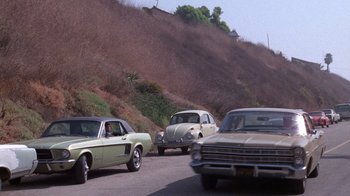 Movie still from “Night Moves” (1975), directed by Arthur Penn – A group of cars driving down a road next to a hill; Wide shot, High angle