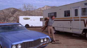 Movie still from “Night Moves” (1975), directed by Arthur Penn – A man holding a dog in front of an rv; Wide shot, Low angle