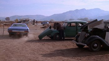 Movie still from “Night Moves” (1975), directed by Arthur Penn – An old green car is being lifted by a man; Wide shot, High angle