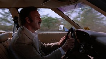 Movie still from “Night Moves” (1975), directed by Arthur Penn – A man in a suit driving a car; Medium shot, Low angle