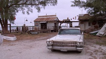 Movie still from “Night Moves” (1975), directed by Arthur Penn – An old car parked in front of an old building; Extreme Wide shot, Low angle
