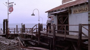 Movie still from “Night Moves” (1975), directed by Arthur Penn – A man standing on a wooden deck near the ocean; Extreme Wide shot, Low angle