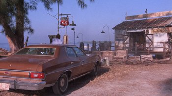 Movie still from “Night Moves” (1975), directed by Arthur Penn – An old car parked in front of a building; Wide shot, Over the shoulder angle
