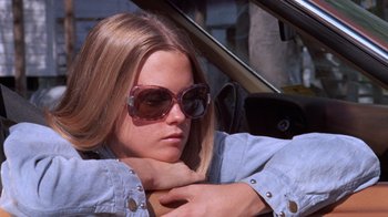 Movie still from “Night Moves” (1975), directed by Arthur Penn – A young woman wearing sunglasses sitting in the driver's seat of a car; Close Up shot, Low angle