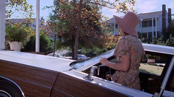 Movie still from “Night Moves” (1975), directed by Arthur Penn – A woman in a pink hat is looking out of a window; Wide shot, Low angle