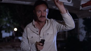 Movie still from “Night Moves” (1975), directed by Arthur Penn – A man holding a gun while standing in a dark room; Close Up shot, Low angle
