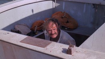 Movie still from “Night Moves” (1975), directed by Arthur Penn – A man with a beard and mustache is in the back of a boat; Medium shot, High angle