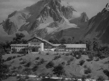 Movie still from “Night Train to Munich” (1940), directed by Carol Reed – A black and white photo of a house with a mountain in the background; Extreme Wide shot, High angle