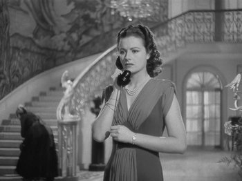 Movie still from “Night Train to Munich” (1940), directed by Carol Reed – A woman talking on a phone while standing next to a staircase; Medium shot, Low angle