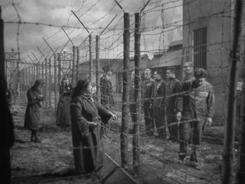 Movie still from “Night Train to Munich” (1940), directed by Carol Reed – A group of people standing around a barbed wire fence; Wide shot, Low angle