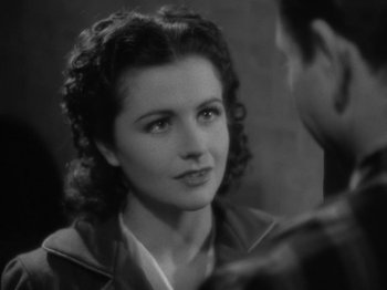 Movie still from “Night Train to Munich” (1940), directed by Carol Reed – An old photo of a woman in a jacket looking at the camera; Close Up shot, Over the shoulder angle