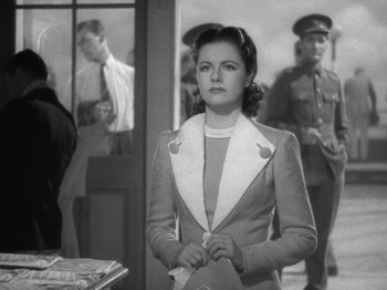 Movie still from “Night Train to Munich” (1940), directed by Carol Reed – A woman standing in front of a group of people; Medium shot, Over the shoulder angle