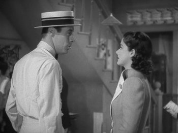 Movie still from “Night Train to Munich” (1940), directed by Carol Reed – A man and a woman standing next to each other in front of a staircase; Medium shot, High angle