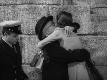 Movie still from “Night Train to Munich” (1940), directed by Carol Reed – A man and a woman hug in front of a stone wall; Medium shot, Over the shoulder angle