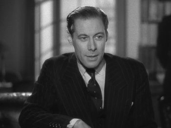 Movie still from “Night Train to Munich” (1940), directed by Carol Reed – A man wearing a suit and tie sitting in a room; Close Up shot, High angle