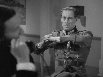 Movie still from “Night Train to Munich” (1940), directed by Carol Reed – A man in a military uniform sitting on a chair; Close Up shot, Over the shoulder angle