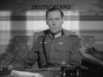 Movie still from “Night Train to Munich” (1940), directed by Carol Reed – A man sitting at a table wearing a military uniform; Close Up shot, Low angle