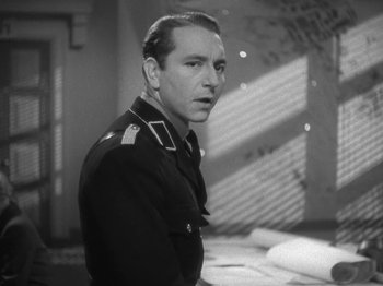 Movie still from “Night Train to Munich” (1940), directed by Carol Reed – A man in a military uniform standing in front of a wall; Close Up shot, Low angle