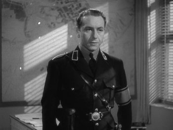 Movie still from “Night Train to Munich” (1940), directed by Carol Reed – A man in a military uniform standing in a room; Medium shot, Low angle