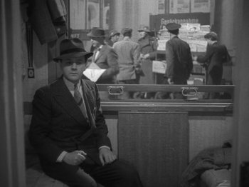 Movie still from “Night Train to Munich” (1940), directed by Carol Reed – A black and white photo of a man in a suit and hat; Medium shot, High angle