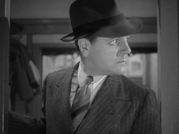 Movie still from “Night Train to Munich” (1940), directed by Carol Reed – A black and white photo of a man in a suit and hat; Close Up shot, Low angle