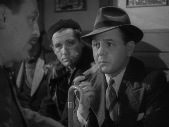 Movie still from “Night Train to Munich” (1940), directed by Carol Reed – A man smoking a pipe while sitting next to another man in a hat; Medium shot, Over the shoulder angle
