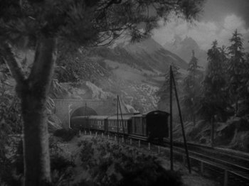 Movie still from “Night Train to Munich” (1940), directed by Carol Reed – A train traveling down tracks next to a forest; Extreme Wide shot, High angle
