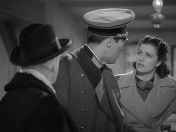 Movie still from “Night Train to Munich” (1940), directed by Carol Reed – A man and a woman talking to a man in a uniform; Medium shot, Over the shoulder angle