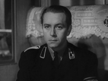 Movie still from “Night Train to Munich” (1940), directed by Carol Reed – A man in a military uniform sitting in a chair; Close Up shot, Low angle