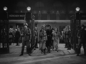 Movie still from “Night Train to Munich” (1940), directed by Carol Reed – A black and white photo of a group of men and women in uniform; Wide shot, Low angle