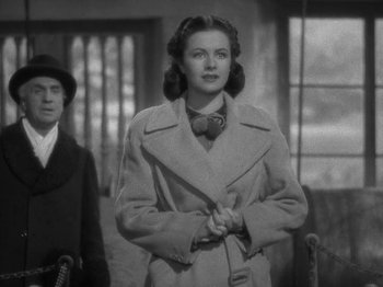 Movie still from “Night Train to Munich” (1940), directed by Carol Reed – A black and white photo of a woman in a trench coat and bow tie; Medium shot, Low angle