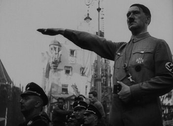 Movie still from “Night and Fog” (1956), directed by Alain Resnais – An old photo of a man in a military uniform pointing; Medium shot, Low angle