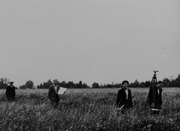 Movie still from “Night and Fog” (1956), directed by Alain Resnais – Two people in a field with a camera and a microphone; Extreme Wide shot, Low angle