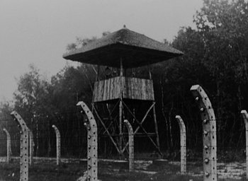 Movie still from “Night and Fog” (1956), directed by Alain Resnais – A black - and - white photo of a tower in the middle of a field; Extreme Wide shot, Low angle