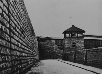 Movie still from “Night and Fog” (1956), directed by Alain Resnais – A black and white photo of a brick wall and a building; Extreme Wide shot, High angle