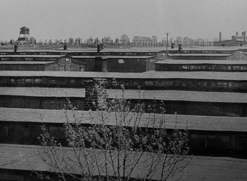 Movie still from “Night and Fog” (1956), directed by Alain Resnais – A black and white photo of a train yard; Extreme Wide shot, High angle