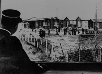 Movie still from “Night and Fog” (1956), directed by Alain Resnais – An old black and white photo of a man looking out of a window; Extreme Wide shot, Over the shoulder angle