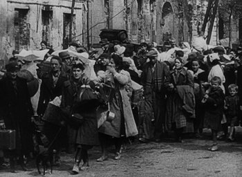 Movie still from “Night and Fog” (1956), directed by Alain Resnais – A group of people standing next to each other on a street; Wide shot, High angle