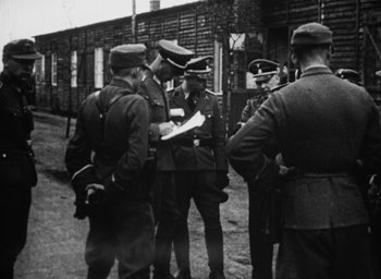 Movie still from “Night and Fog” (1956), directed by Alain Resnais – A black and white photo of a group of men in uniform; Medium shot, Over the shoulder angle