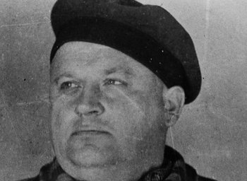 Movie still from “Night and Fog” (1956), directed by Alain Resnais – An old black and white photo of a man wearing a hat; Close Up shot, Low angle